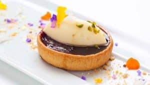 Saborea una tarta adornada con helado de vainilla, pétalos de flores y nueces trituradas en un plato blanco impecable en el Restaurante Las Corchuelas Hospes Palacio de Arenales en Cáceres. - ForTwo - Planes para parejas