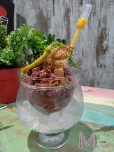 En el Restaurante Mario & Marieta de Cáceres, un tartar de ternera con guindilla, chicharrones y una pipeta rellena de salsa se presenta elegantemente en copa con hielo y con una planta realzando sutilmente la escena. - ForTwo - Planes para parejas