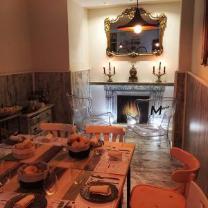 El Restaurante Mario & Marieta en Cáceres cuenta con un acogedor comedor con una mesa rústica, chimenea, un espejo ornamentado y sillas transparentes. La cálida iluminación realza la elegante decoración. - ForTwo - Planes para parejas