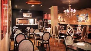 El elegante interior del Restaurante Milo Grill en Barcelona exhibe sillas estampadas, un piso de madera, una cocina abierta y una impresionante lámpara de araña. - ForTwo - Planes para parejas