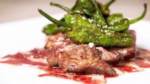 En el Restaurante Milo Grill de Barcelona, disfrute de una carne preparada a la parrilla, adornada con pimientos verdes y servida con estilo en un plato blanco. - ForTwo - Planes para parejas