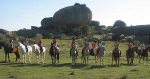 Un grupo de caballos posa frente a grandes rocas en un prado, realzando la belleza del paisaje de la dehesa cacereña. Disfruta de esta ruta con "Ruta a caballo por la dehesa extremeña (Cáceres)". - ForTwo - Planes para parejas
