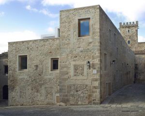 El encanto histórico de Cáceres queda plasmado en el Hotel Atrio, un edificio de piedra con ventanas rectangulares y una torre tipo castillo bajo un cielo parcialmente nublado. - ForTwo - Planes para parejas