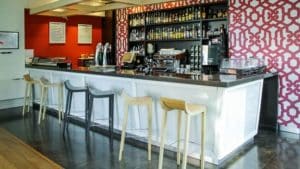 El restaurante Eustaquio Blanco en Cáceres cuenta con una moderna barra con una pared con dibujos rojos, un elegante mostrador blanco, taburetes de madera y estantes llenos de diversas botellas. - ForTwo - Planes para parejas