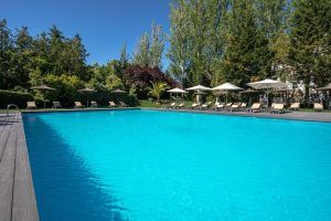 El Hotel Barceló V Centenario de Cáceres cuenta con una piscina al aire libre rodeada de tumbonas y árboles, todo ello bajo un cielo azul claro. - ForTwo - Planes para parejas
