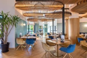 Un moderno restaurante en el elegante Hotel Barceló V Centenario (Cáceres) cuenta con interiores de madera, un diseño de techo único y mesas dispuestas con sillas azules y beige. - ForTwo - Planes para parejas