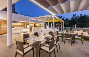Ubicado en el encantador ambiente de Cáceres, el restaurante al aire libre del Hotel Barceló V Centenario presenta mesas elegantemente dispuestas, sillas de mimbre, una decoración contemporánea y una acogedora iluminación nocturna. - ForTwo - Planes para parejas