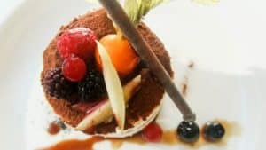 Disfrute de un postre de lujo en el Restaurante Eustaquio Blanco (Cáceres), con frutos rojos, naranja, palito de chocolate, hojas verdes y nata, todo ello elegantemente dispuesto en un plato blanco. - ForTwo - Planes para parejas