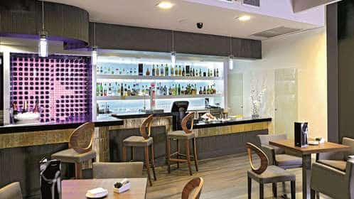 Explore el moderno y elegante bar del Sercotel Gran Luna de 4*, realzado por elegantes tronas y una variedad de botellas. Mejore su visita con acceso completo al lujoso gimnasio y spa, que le ofrece una experiencia completa. Nombre del producto: Escapada con spa y gimnasio en el hotel Sercotel Gran Luna de 4*. - ForTwo - Planes para parejas