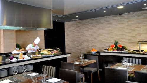 En la vibrante cocina del Hotel Sercotel Gran Luna de 4*, el chef prepara con maestría los platos mientras los huéspedes disfrutan de un bufé repleto de frutas y verduras frescas. Los visitantes pueden relajarse en el spa o recargar energías en el gimnasio durante su "Escapada con spa y gimnasio". - ForTwo - Planes para parejas