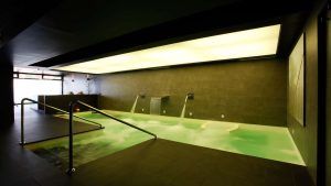Disfrute de la moderna piscina interior del Hotel Sinagoga, con iluminación cenital, chorros de agua y elegantes paredes de azulejos oscuros. No pierda la oportunidad de darse un refrescante chapuzón antes del desayuno durante su escapada con desayuno, chocolates y acceso al spa en Hervás. - ForTwo - Planes para parejas