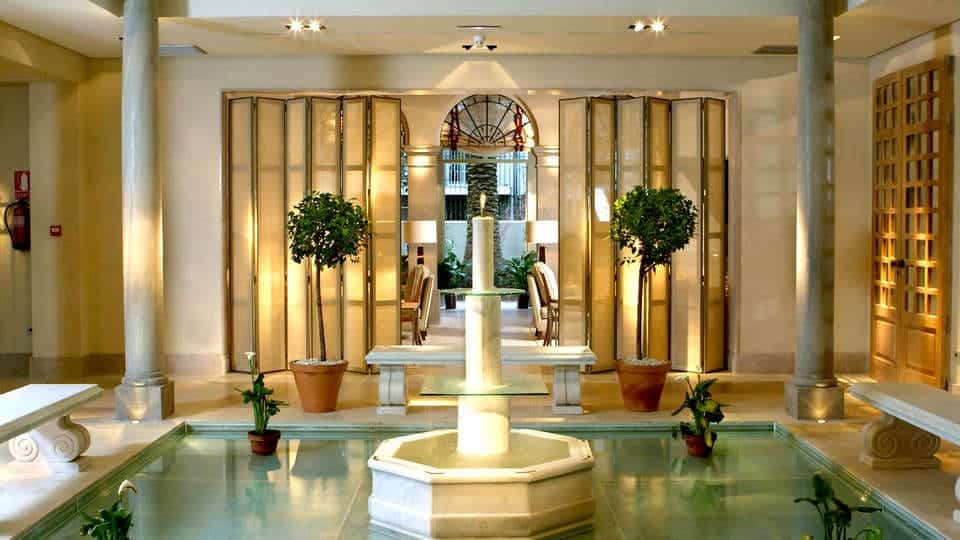 Experimente el elegante lobby del Hotel Villa Oniria con su fuente central, árboles en macetas e iluminación suave, perfecto para una "Escapada romántica con spa en hotel Villa Oniria 4 estrellas (Granada). - ForTwo - Planes para parejas