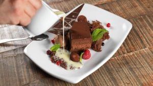 Rociar crema sobre un delicioso postre de chocolate, adornado con bayas y menta, crea una obra maestra visual en un plato blanco, evocando una experiencia de la vibrante cocina del Restaurante Mastropiero Gastrobar (Cáceres). - ForTwo - Planes para parejas