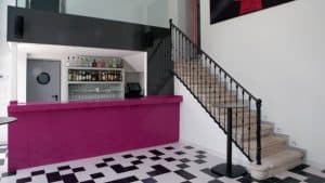 El moderno interior del Restaurante Mastropiero Gastrobar (Cáceres) muestra una barra rosa, un suelo a cuadros blancos y negros y una escalera con una elegante barandilla negra. - ForTwo - Planes para parejas