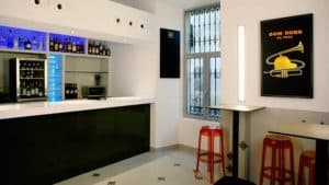 El Restaurante Mastropiero Gastrobar en Cáceres cuenta con un interior moderno con estantes de botellas, un elegante póster de pared y taburetes rojos junto a mesas acogedoras, que brindan ambiente y deleite culinario. - ForTwo - Planes para parejas