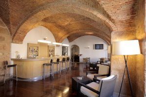Descubra un acogedor bar en el encantador Hotel NH Collection Palacio de Oquendo en Cáceres. Con su techo abovedado de ladrillo, suelos de madera y una atractiva barra con taburetes, combina a la perfección comodidad y encanto. - ForTwo - Planes para parejas