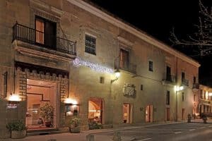 Por la noche, el histórico edificio de piedra de Cáceres resalta con elegancia, con sus balcones iluminados bajo el cartel iluminado del Hotel NH Collection Palacio de Oquendo (Cáceres). - ForTwo - Planes para parejas