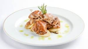 En el Restaurante Torreorgaz Parador de Cáceres, un plato blanco presenta un plato gourmet de carne estofada sobre patatas en rodajas, adornado con una ramita de romero. - ForTwo - Planes para parejas