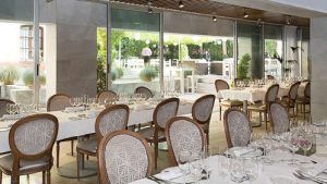El elegante comedor del Hotel Palacio de los Patos, parte de la "Escapada de lujo en el hotel Palacio de los Patos con spa incluido (Granada)", exhibe manteles blancos, sillas ornamentadas y paredes de vidrio con vistas al jardín, que personifican el verdadero lujo. - ForTwo - Planes para parejas