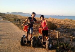 Dos amigos con casco posan en Segways por un sendero costero bajo un cielo despejado, disfrutando de su aventura Ruta en Segway en los arrozales de Pals. - ForTwo - Planes para parejas
