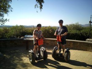 Dos amigos con casco disfrutan de una Ruta en Segway por los arrozales de Pals, rodeados de frondosos árboles y lejanas montañas al fondo. - ForTwo - Planes para parejas