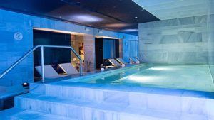 Disfrute de la elegancia de una piscina spa cubierta en nuestra Escapada de lujo en el hotel Palacio de los Patos con spa incluido (Granada), con una relajante iluminación azul, paredes de mármol, tumbonas y escalones que conducen al agua relajante para una relajación máxima. - ForTwo - Planes para parejas