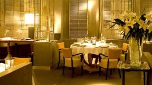 El Hotel Villa Oniria ofrece un elegante ambiente de restaurante con iluminación tenue, una mesa redonda con mantel blanco, sillas y lirios blancos, ideal para la "Escapada romántica con spa en hotel Villa Oniria 4 estrellas (Granada). - ForTwo - Planes para parejas