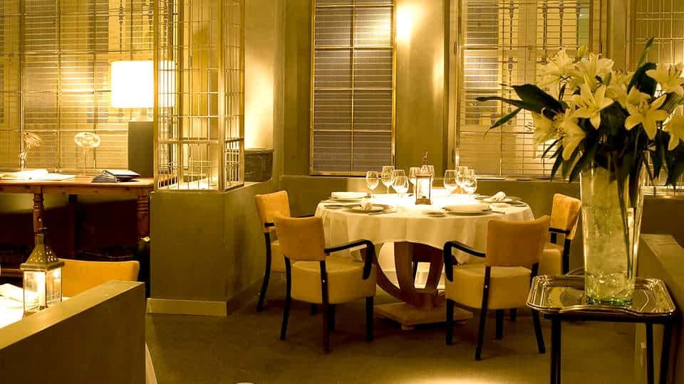 El Hotel Villa Oniria ofrece un elegante ambiente de restaurante con iluminación tenue, una mesa redonda con mantel blanco, sillas y lirios blancos, ideal para la "Escapada romántica con spa en hotel Villa Oniria 4 estrellas (Granada). - ForTwo - Planes para parejas