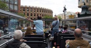 Los pasajeros disfrutan de las vistas desde un autobús descapotable en Valencia, con un telón de fondo que recuerda al Coliseo. Las entradas para el autobús turístico de Valencia ofrecen una experiencia inolvidable para los exploradores más apasionados. - ForTwo - Planes para parejas