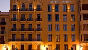 La fachada del Hotel Zenit, en el casco histórico de Valencia, se ilumina cálidamente al atardecer, iluminando sus pintorescos balcones. Disfruta de ello con el paquete Escapada Hotel Zenit, que incluye una visita guiada al casco histórico, paella, acceso a la sauna y gimnasio. - ForTwo - Planes para parejas