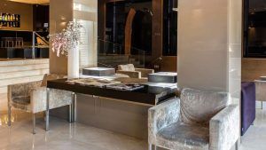 Bienvenido al Hotel Zenit en Valencia, donde un moderno vestíbulo con lujosos sillones, un escritorio negro y arreglos florales preparan el escenario para tu experiencia Escapada Hotel Zenit + visita guiada al casco histórico + paella + sauna + gimnasio. - ForTwo - Planes para parejas