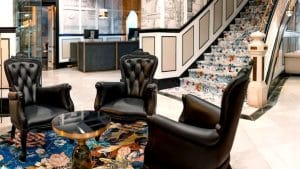 Experimente el elegante vestíbulo de Escapada SH Inglés Boutique + desayuno (Valencia), con tres sillas negras, una alfombra floral y una escalera ornamentada. Perfecto para su próxima escapada o para disfrutar de un desayuno relajado con estilo. - ForTwo - Planes para parejas