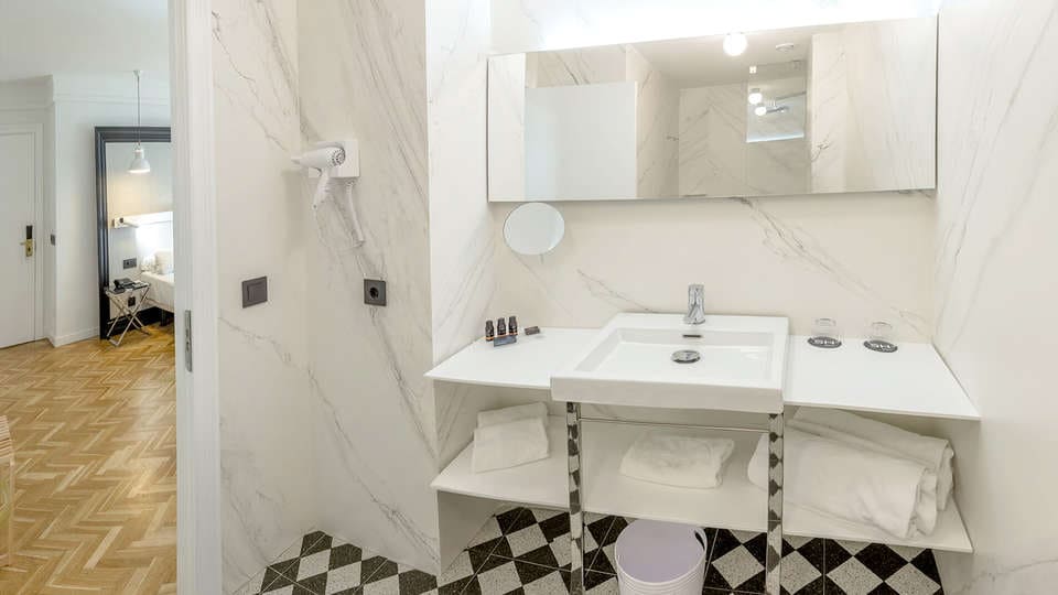Transforma tu baño en una moderna Escapada SH Inglés Boutique + desayuno, con un lavabo blanco impecable, espejo, toallas de lujo y artículos de aseo. Los azulejos con motivos geométricos añaden un toque sofisticado a este refugio de inspiración valenciana. - ForTwo - Planes para parejas