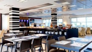 La Escapada ofrece desayuno en un ambiente amplio y luminoso en el moderno restaurante del Gran Casino Aljarafe, equipado con una elegante zona de buffet, mesas perfectamente dispuestas y columnas a rayas. - ForTwo - Planes para parejas