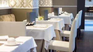 El menú del Restaurante Ampar-Palau de la Mar en Valencia ofrece un ambiente elegante con mesas cuidadosamente dispuestas con manteles blancos y sillas acolchadas. - ForTwo - Planes para parejas