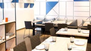 El moderno interior del restaurante Valencia presenta paredes con diseños geométricos, mesas de madera, sillas grises y una cristalería impecablemente dispuesta. Inspirado en la elegancia clásica del Restaurante Griego Kuzina, realza cada experiencia gastronómica. - ForTwo - Planes para parejas