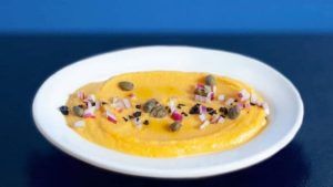 Un plato blanco del Restaurante griego Kuzina (Valencia) muestra puré de papas cremoso adornado con cebolla picada, alcaparras y aceitunas en rodajas. - ForTwo - Planes para parejas
