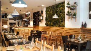 El restaurante Galipán en Valencia cuenta con un interior moderno con mesas de madera, una exuberante pared verde, luces colgantes y mesas elegantemente dispuestas con copas de vino. - ForTwo - Planes para parejas