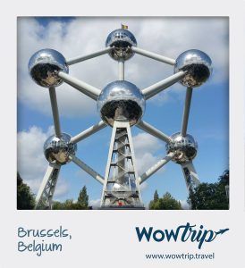 El Atomium de Bruselas, un imponente monumento de esta vibrante ciudad europea, se alza imponente contra un cielo azul con tenues nubes y está rodeado de frondosos árboles. Vívelo con nuestro "Viaje sorpresa con vuelo + hotel a una ciudad europea". - ForTwo - Planes para parejas