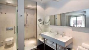 Transforma tu baño en una escapada elegante con el estilo de Hospes Palau de la Mar: con ducha, inodoro, lavabo doble, espejo grande para reflejar la luz natural y lujosas toallas en el estante: un toque perfecto del lujo de Valencia. - ForTwo - Planes para parejas