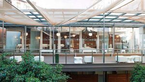 El moderno edificio de cristal, con amplios ventanales y elegantes marquesinas, se alza elegantemente entre exuberantes plantas, haciéndose eco de la estética tranquila de Escapada Hospes Palau de la Mar con desayuno y spa (Valencia). - ForTwo - Planes para parejas