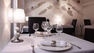El comedor suavemente iluminado de La Bodeguita de María en Valencia ofrece una elegante disposición con copas de vino, platos y una lámpara. - ForTwo - Planes para parejas