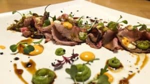 En el Restaurante Galipán (Valencia), saboree rodajas de carne de res aderezadas con salsa verde, microvegetales y porciones de naranja que reflejan la rica herencia culinaria de Valencia. - ForTwo - Planes para parejas
