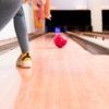 Una persona lanza hábilmente una bola roja por la pista de madera pulida mientras disfruta de Bowling en Barcelona - Partida de bolos en Barcelona. - ForTwo - Planes para parejas