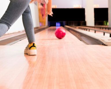 Una persona lanza hábilmente una bola roja por la pista de madera pulida mientras disfruta de Bowling en Barcelona - Partida de bolos en Barcelona. - ForTwo - Planes para parejas