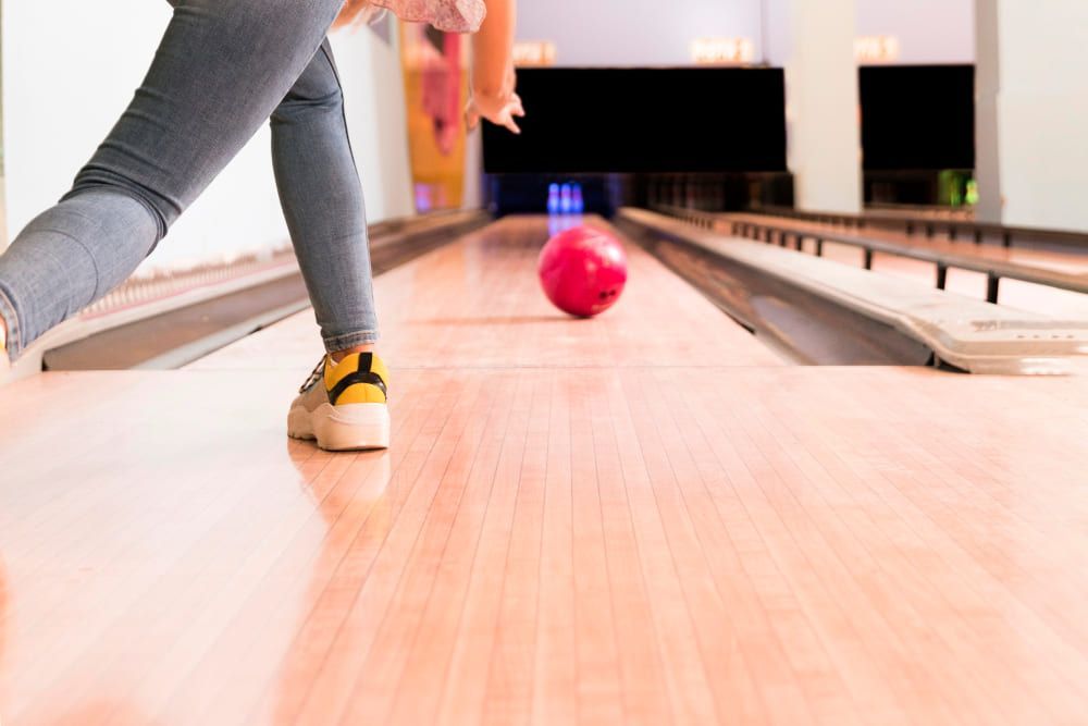 Una persona lanza hábilmente una bola roja por la pista de madera pulida mientras disfruta de Bowling en Barcelona - Partida de bolos en Barcelona. - ForTwo - Planes para parejas