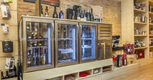 Explora el interior moderno de una tienda de vinos con refrigeradores con frente de vidrio y estantes de madera que exhiben diferentes vinos, ideal para una experiencia de "Cata de vermuts con aperitivo en Di-Ví (Barcelona)" que refleja la atmósfera vibrante de Barcelona. - ForTwo - Planes para parejas