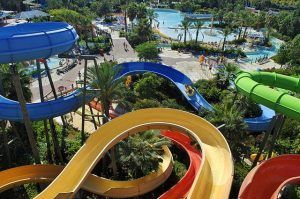 Vista aérea del Caribe Aquatic Park en Port Aventura en Tarragona con coloridos toboganes que serpentean entre exuberante vegetación y una piscina de olas. - ForTwo - Planes para parejas