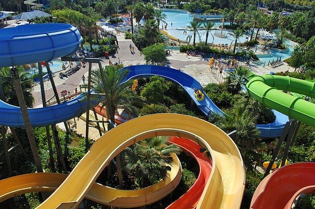 Vista aérea del Caribe Aquatic Park en Port Aventura en Tarragona con coloridos toboganes que serpentean entre exuberante vegetación y una piscina de olas. - ForTwo - Planes para parejas