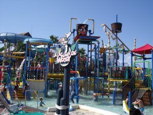 Vive el ambiente vibrante de Caribe Aquatic Park, Port Aventura en Tarragona, con coloridos toboganes y estructuras de escalada entre salpicaduras de agua y rodeado de gente disfrutando de la diversión. - ForTwo - Planes para parejas
